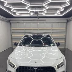 the front end of a white car in a garage with lights on and overhead lighting