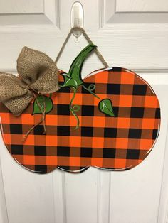 an orange and black pumpkin door hanger with a burluck bow on it