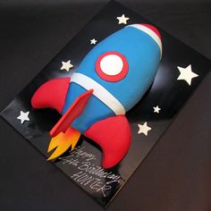 a cake shaped like a rocket ship on top of a black surface with stars around it