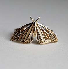 a close up of a butterfly shaped ring on a white surface with one wing extended