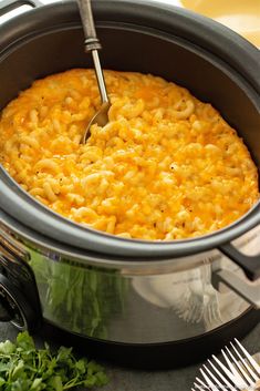 a pot filled with macaroni and cheese on top of a table next to silverware