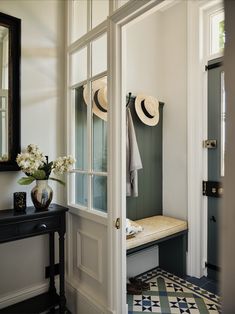 there is a bench with hats on it in the entry way and a vase filled with flowers