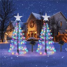 three christmas trees in front of a house decorated with lights and snowflakes at night