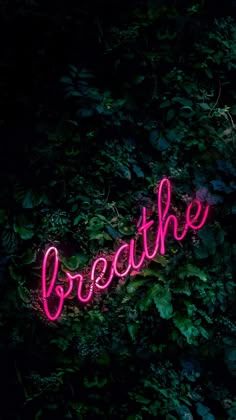 a pink neon sign that says breathe in front of some green bushes and trees at night