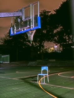 a basketball hoop with a chair in front of it on an outdoor court at night