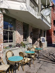 there are many chairs and tables on the sidewalk outside of this building with a clock in the window