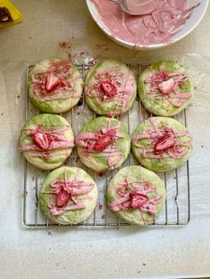 some cookies with pink icing on them sitting on a cooling rack next to a bowl