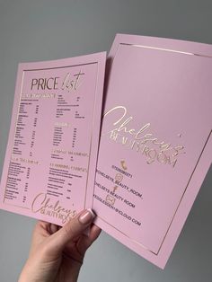 a person holding up two pink menus with gold foil lettering on the front and back