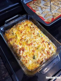 two trays of food sitting on top of an oven with crackers and cheese