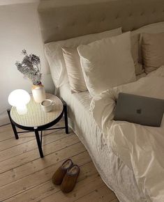 a laptop computer sitting on top of a bed next to a night stand and lamp