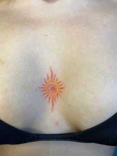 a close up of a woman's breast with an orange sun tattoo on it