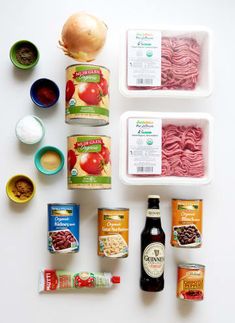 the ingredients for an italian pasta dish laid out on a white surface, including tomatoes, onions, meats and sauces