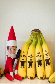 an elf is sitting next to bananas with faces drawn on them and the other two are holding pens