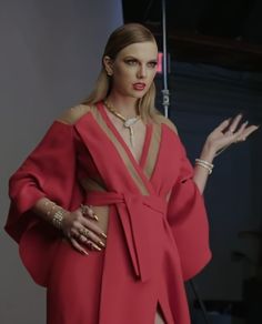 a woman in a red dress is holding her hands out to the side while wearing gold jewelry