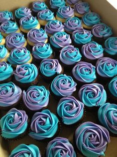 a box filled with blue and purple cupcakes on top of a table next to a phone