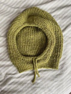 a green knitted hat laying on top of a white bed sheet with a knot at the end