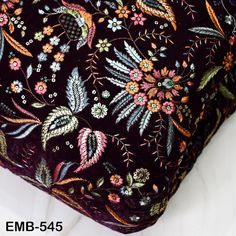 a close up of a pillow on a bed with flowers and leaves printed on it