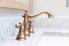 a gold faucet in a white bathroom with marble counter tops and tile backsplash