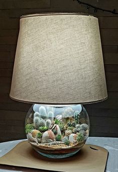 a lamp that is on top of a table with rocks and plants in it next to a sheet of paper