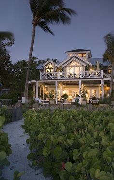 a large white house sitting on top of a lush green field next to palm trees