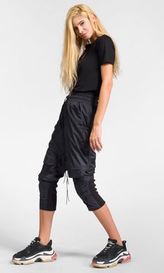 Cropped track pants with knee flap details, made of lightweight polyester fabric for a modern and comfy look. Details: * Elastic waistband with elastic drawstrings and stoppers * Front zipper closure * Decorative knee flaps * Elastic ribbed details * Two front pockets and two back zippered pockets * Calf width adjustment via Velcro patches Stretch Streetwear Cargo Pants With Drawstring, Stretch Ankle-length Cargo Pants For Streetwear, Sporty Cargo Long Pants, Sporty Cargo Style Sweatpants, Sporty Cargo Style Long Pants, Stretch Cargo Pants With Drawstring For Sports, Sporty Stretch Parachute Pants With Drawstring, Urban Stretch Bottoms For Workout, Urban Style Stretch Bottoms For Workout