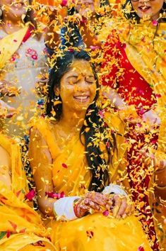 two women are covered in yellow powder and confetti as they sit on the ground