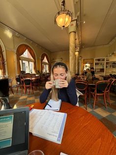 a woman sitting at a table drinking from a cup