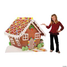 a woman standing next to a gingerbread house