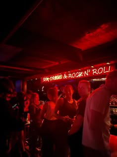 a group of people at a bar with neon signs on the ceiling and red lighting