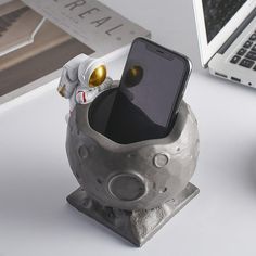 a cell phone holder in the shape of an astronaut's helmet sits on a desk next to a laptop