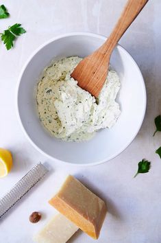 a wooden spoon in a white bowl next to some cheese and lemons on a table