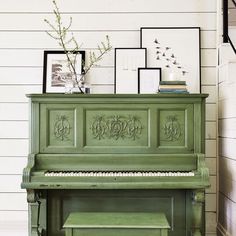 an old green piano in a room with pictures on the wall and a bench next to it