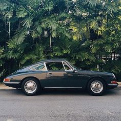 a black porsche sits parked in front of some trees