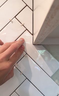 a person's hand is on the edge of a white tile wall with black lines