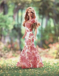 a barbie doll wearing a pink and white dress in the grass with trees behind her