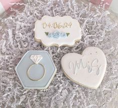 three decorated cookies in the shape of heart, ring and engagement rings on top of shredded paper