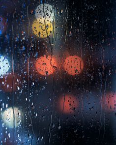 rain drops on the window as cars pass by in the street at night with traffic lights