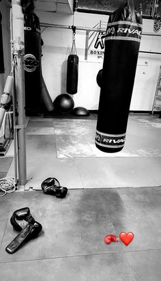 two boxing gloves laying on the ground in front of a punching bag and other equipment