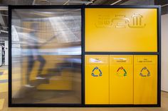 a train station with yellow and black lockers on the wall, people walking in the background