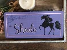 a purple sign that says shade with a horse on it next to some flowers and a candle