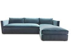 a blue sectional couch sitting on top of a white floor next to a footstool