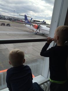 two young boys looking out an airport window at planes on the tarmac behind them