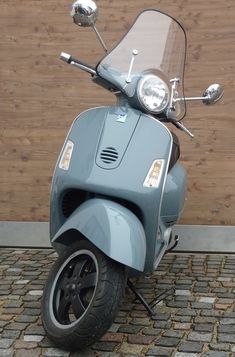 a blue scooter parked next to a wooden wall on cobblestone pavement