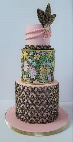 a three tiered cake with flowers and leaves on it's side, sitting on top of a pink plate