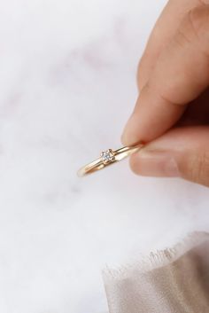 a hand holding a diamond ring on top of a white cloth with it's fingers