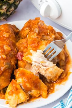 a white plate topped with meat and sauce next to a pineapple on a table