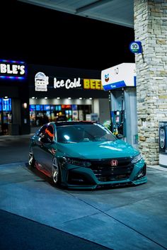 a blue car is parked in front of a gas station at night with the lights on