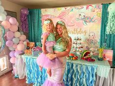 two women standing in front of a table with cake and balloons on it at a mermaid themed birthday party