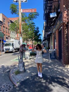 a woman standing on the side of a street next to a pole with a sign