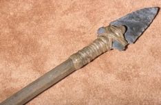 an old metal knife with a wooden handle on a brown carpeted floor in front of a tan background